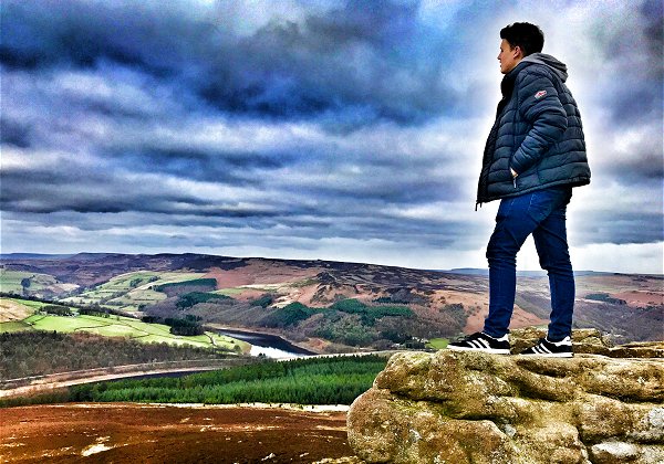 Portrait of young man stood on clifftop overlooking the Peak District