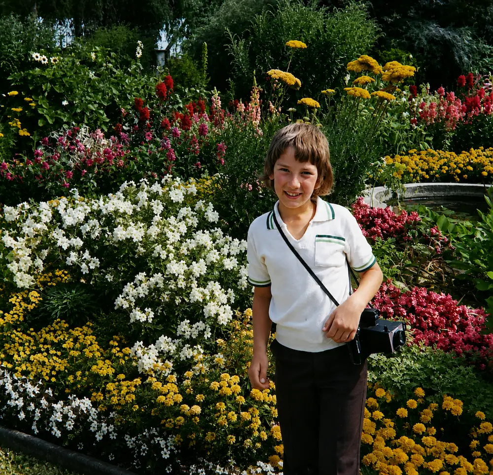 Paul as a child with a camera, surrounded by colourful flowers